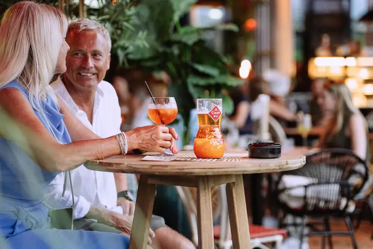 Zwei Spritzer auf einem Tisch, dahinter ein lachendes Paar