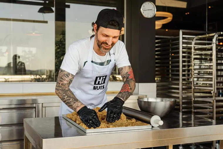 Bäcker mit tätowierten Armen knetet Teig in einer Backstube