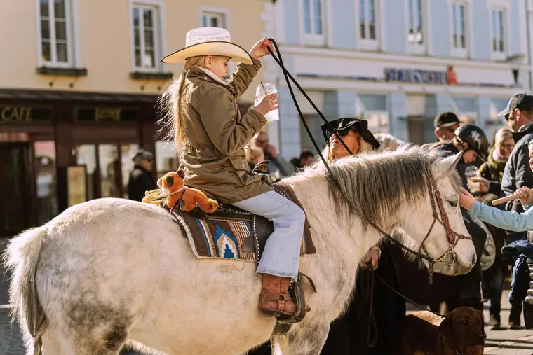 Mädchen mit Cowboyhut sitzt auf einem weißen Pferd beim Ortsumzug