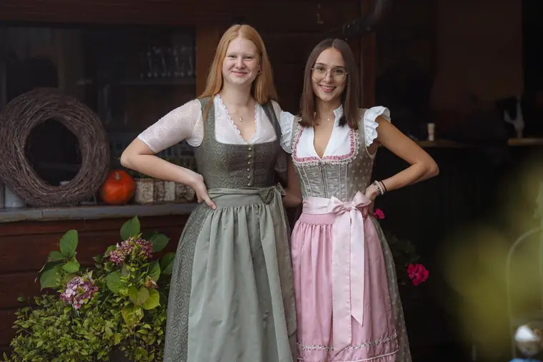 Zwei junge Frauen im Dirndl vor einer Holzhütte