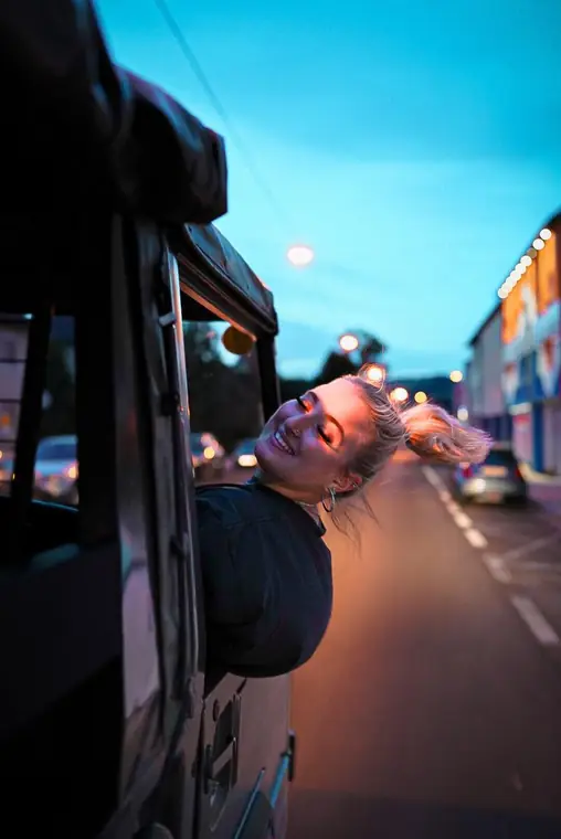 Frau hält ihr Gesicht aus dem Fenster eines fahrenden Busses