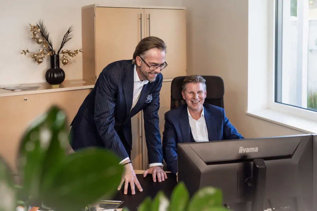 Helmut Hemmelmeir und sein Kollege lachend am Bildschirm im Büro von Lucrum Invest